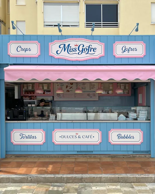 Fachada de Miss Gofre en azul pastel, con rótulos enmarcados en rosa y blanco, toldo rosa y mostrador abierto.