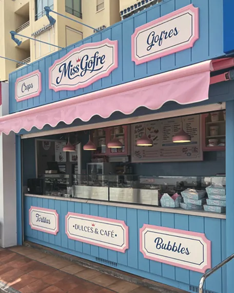 Fachada vintage de una gofrería con revestimiento azul, molduras rosas, rótulos decorativos y toldo de estilo retro.