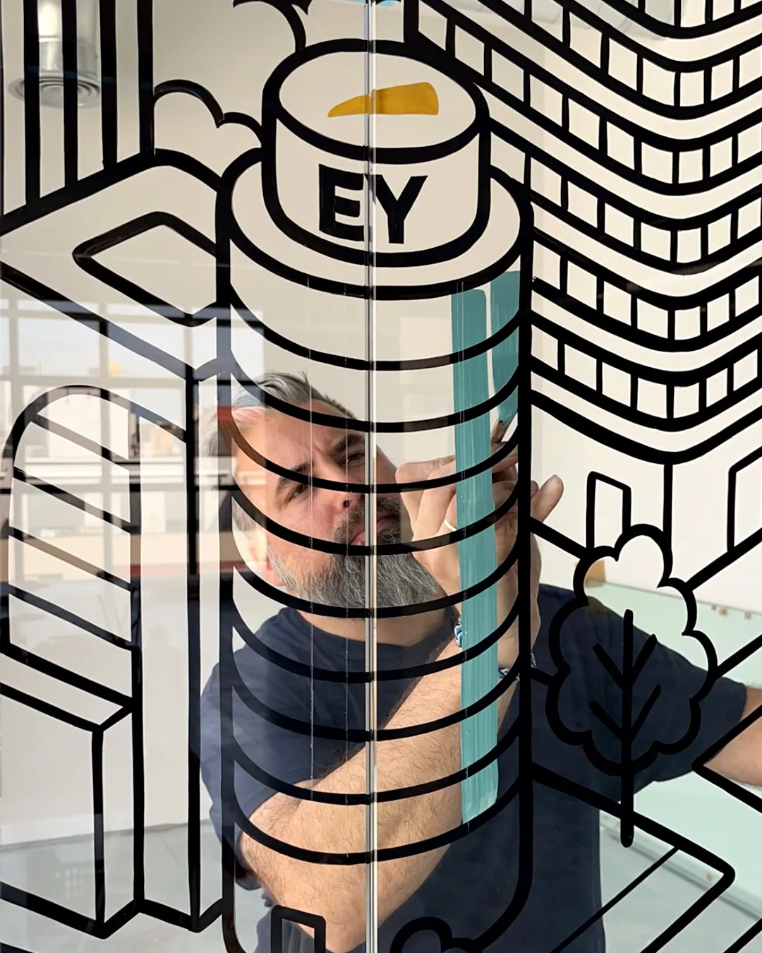 Rotulista pintando a pincel una ilustración sobre vidrio, con edificios delineados en negro y detalles de color.